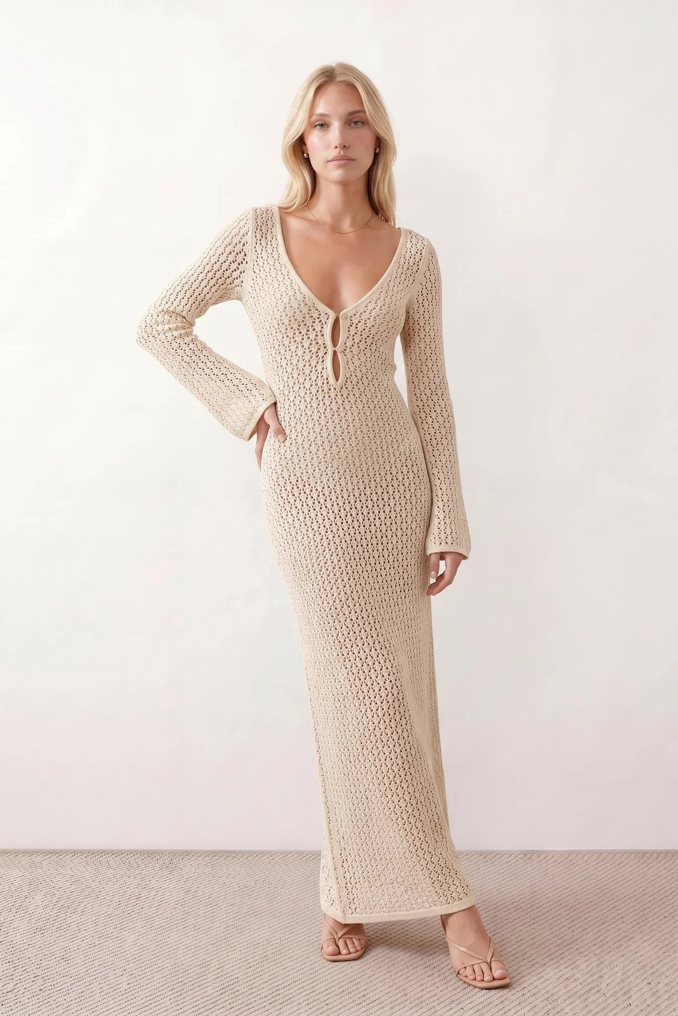 Woman wearing the Calixta Crochet Plunge Neck Maxi Dress in an elegant open-knit crochet design with a deep plunge V-neck, keyhole detail, long flared sleeves, low open back and fitted floor-length silhouette, ideal for beach holidays, festivals and summer occasion wear.