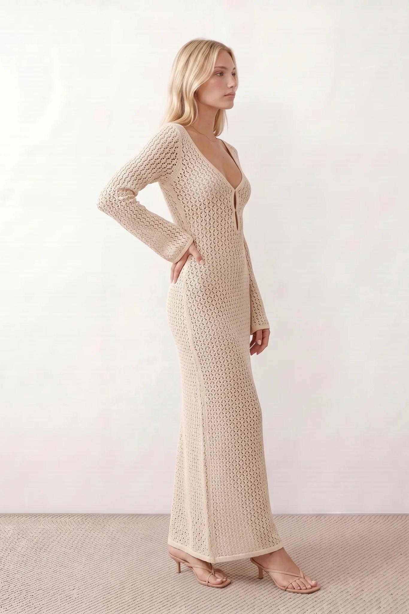 Woman wearing the Calixta Crochet Plunge Neck Maxi Dress in an elegant open-knit crochet design with a deep plunge V-neck, keyhole detail, long flared sleeves, low open back and fitted floor-length silhouette, ideal for beach holidays, festivals and summer occasion wear.