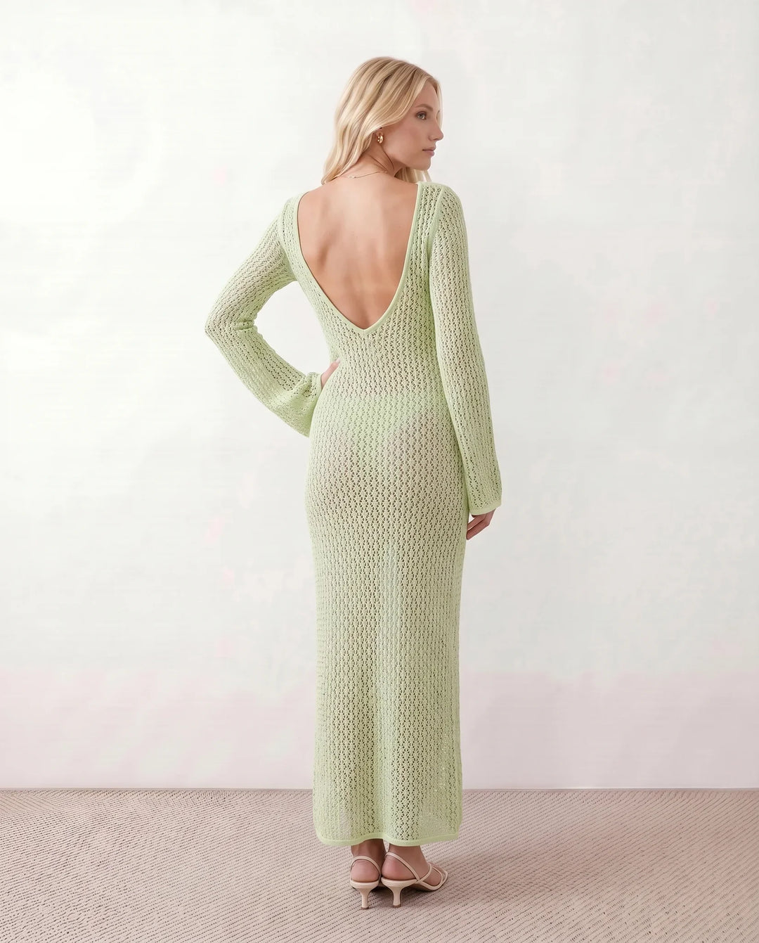 Woman wearing the Calixta Crochet Plunge Neck Maxi Dress in an elegant open-knit crochet design with a deep plunge V-neck, keyhole detail, long flared sleeves, low open back and fitted floor-length silhouette, ideal for beach holidays, festivals and summer occasion wear.