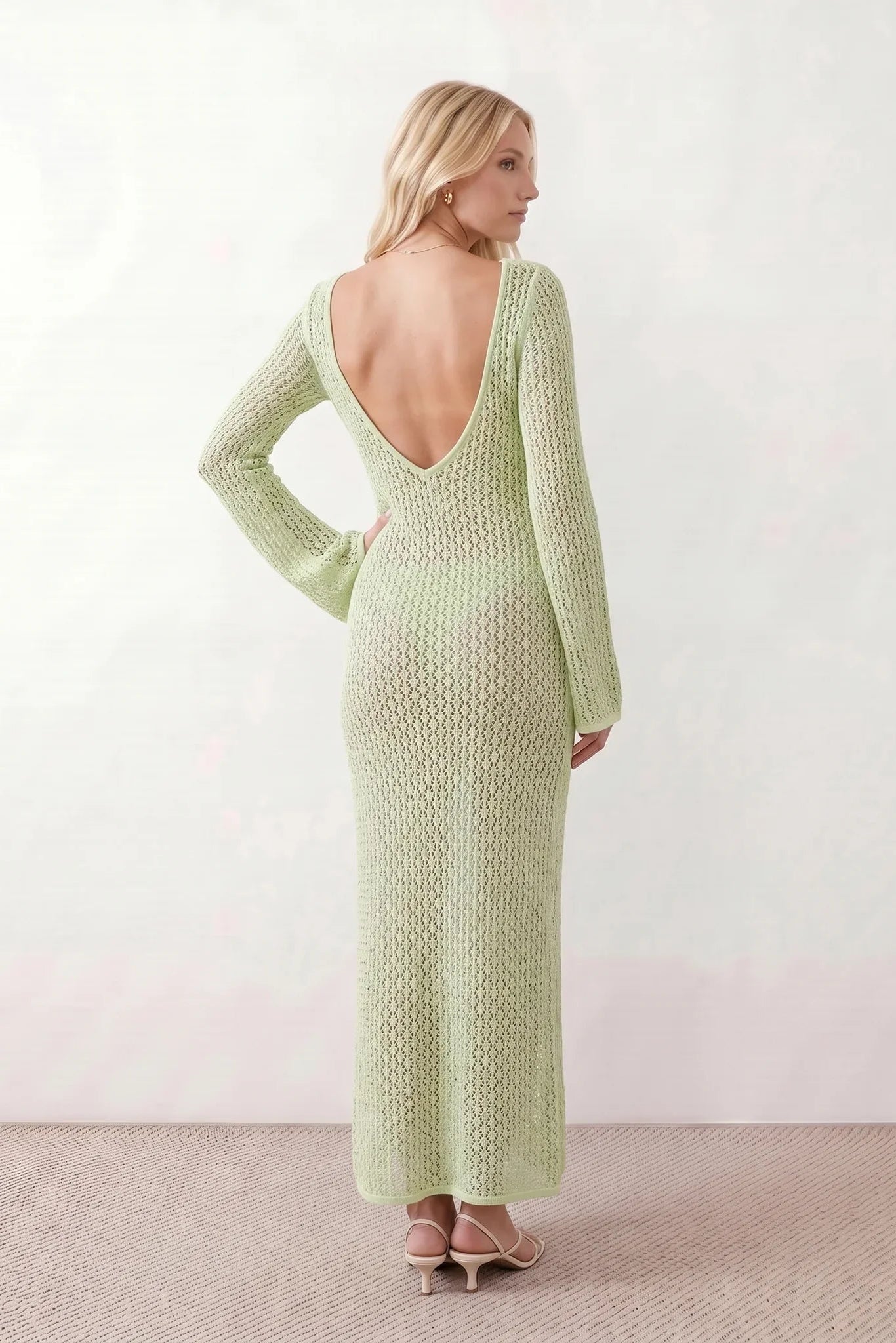 Woman wearing the Calixta Crochet Plunge Neck Maxi Dress in an elegant open-knit crochet design with a deep plunge V-neck, keyhole detail, long flared sleeves, low open back and fitted floor-length silhouette, ideal for beach holidays, festivals and summer occasion wear.