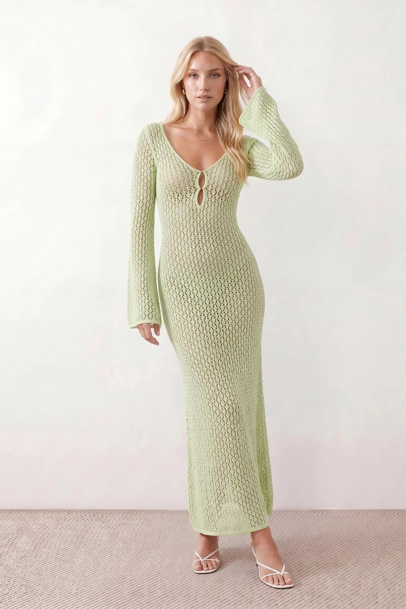 Woman wearing the Calixta Crochet Plunge Neck Maxi Dress in an elegant open-knit crochet design with a deep plunge V-neck, keyhole detail, long flared sleeves, low open back and fitted floor-length silhouette, ideal for beach holidays, festivals and summer occasion wear.