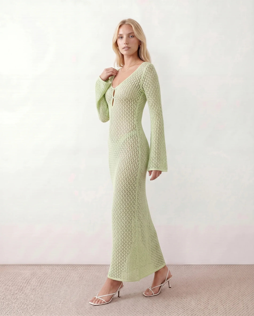 Woman wearing the Calixta Crochet Plunge Neck Maxi Dress in an elegant open-knit crochet design with a deep plunge V-neck, keyhole detail, long flared sleeves, low open back and fitted floor-length silhouette, ideal for beach holidays, festivals and summer occasion wear.