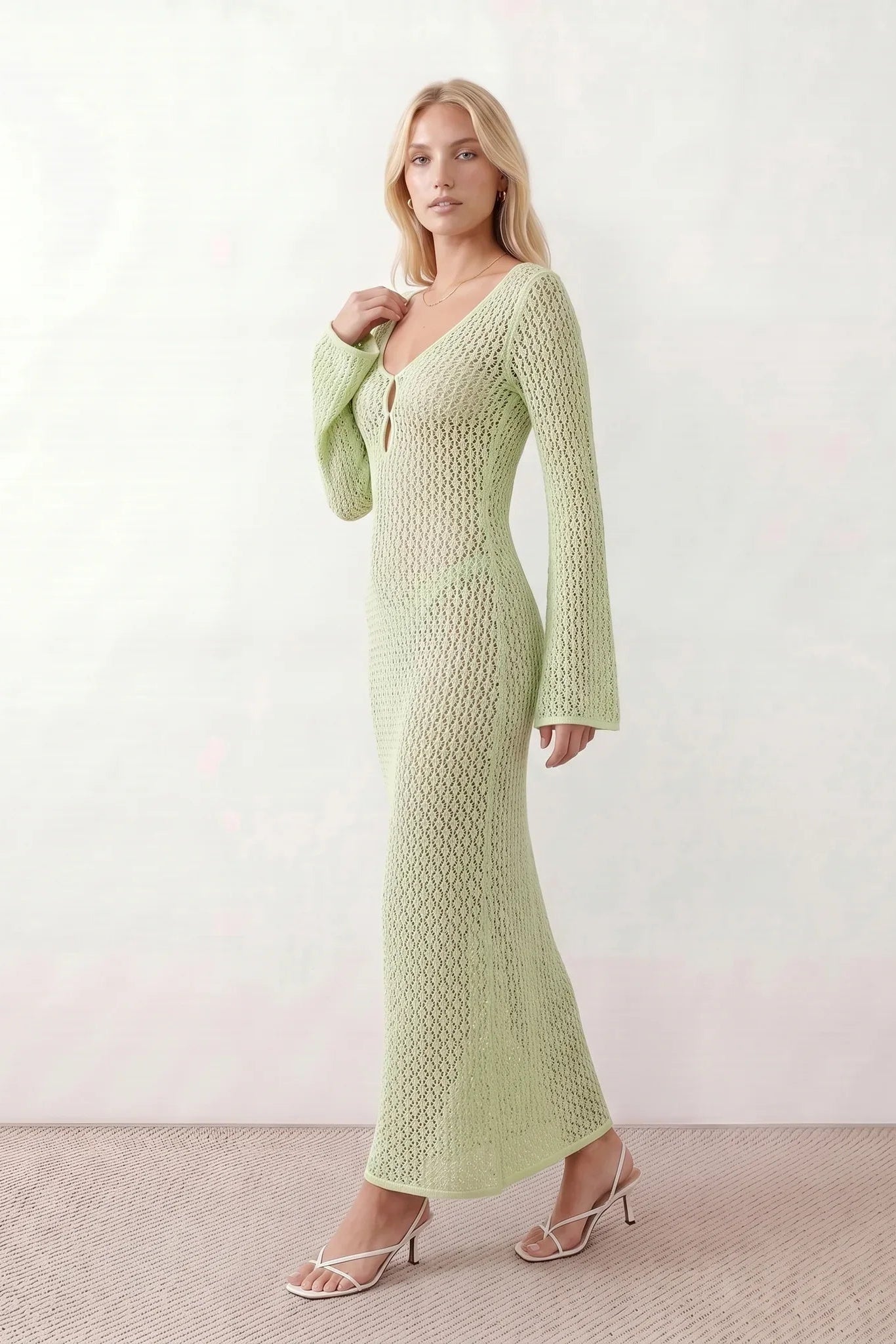 Woman wearing the Calixta Crochet Plunge Neck Maxi Dress in an elegant open-knit crochet design with a deep plunge V-neck, keyhole detail, long flared sleeves, low open back and fitted floor-length silhouette, ideal for beach holidays, festivals and summer occasion wear.
