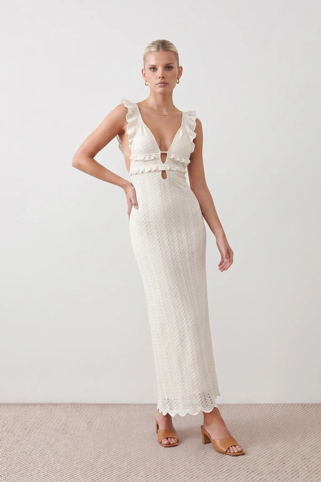 Woman wearing the crochet mermaid maxi dress featuring an intricate crochet knit, plunging V-neckline, ruffled shoulder straps, keyhole waist cut-out, adjustable lace-up open back, scalloped hem, and a figure-hugging maxi silhouette, ideal for weddings, cocktail parties, and elegant evening occasions.