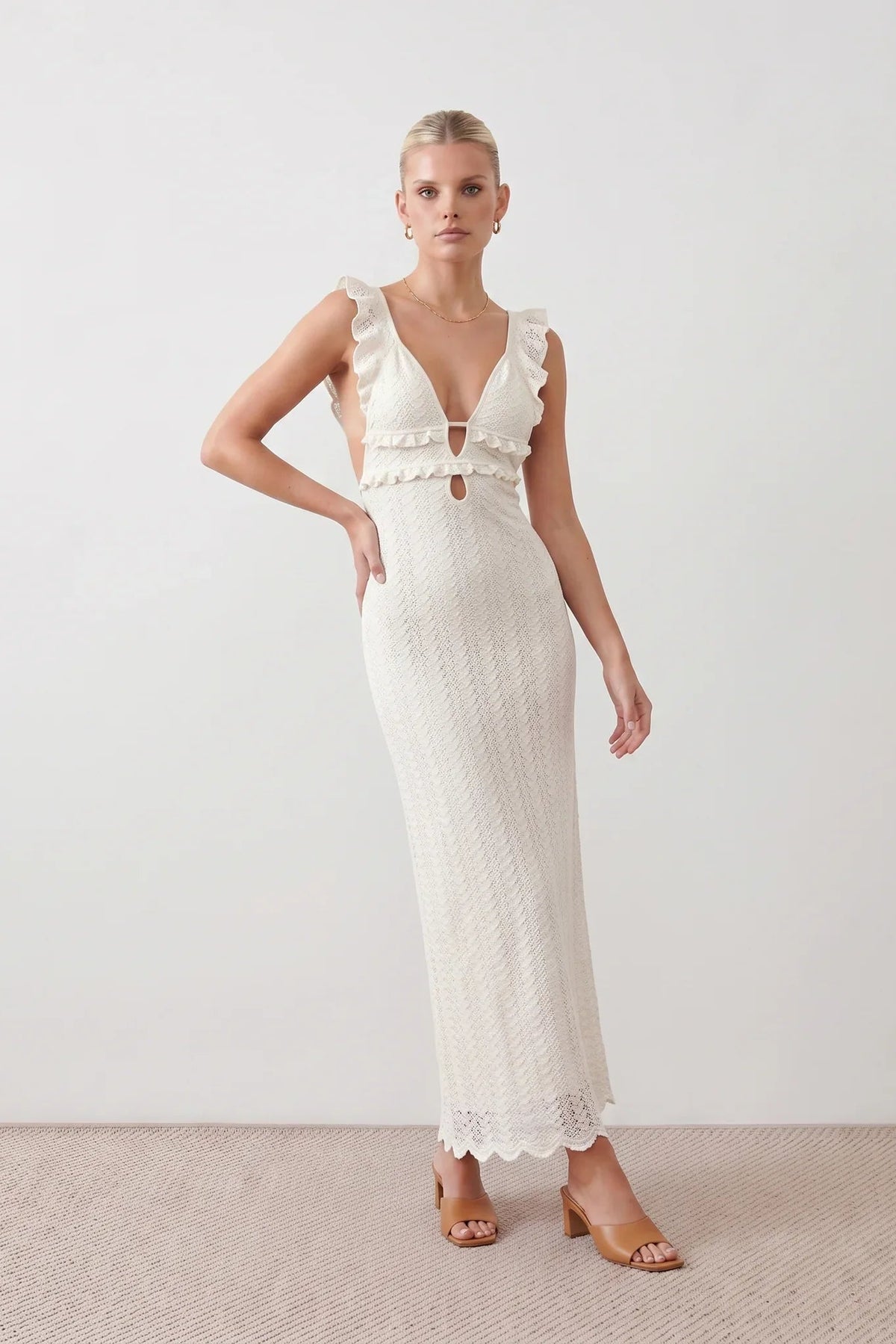 Woman wearing the crochet mermaid maxi dress featuring an intricate crochet knit, plunging V-neckline, ruffled shoulder straps, keyhole waist cut-out, adjustable lace-up open back, scalloped hem, and a figure-hugging maxi silhouette, ideal for weddings, cocktail parties, and elegant evening occasions.