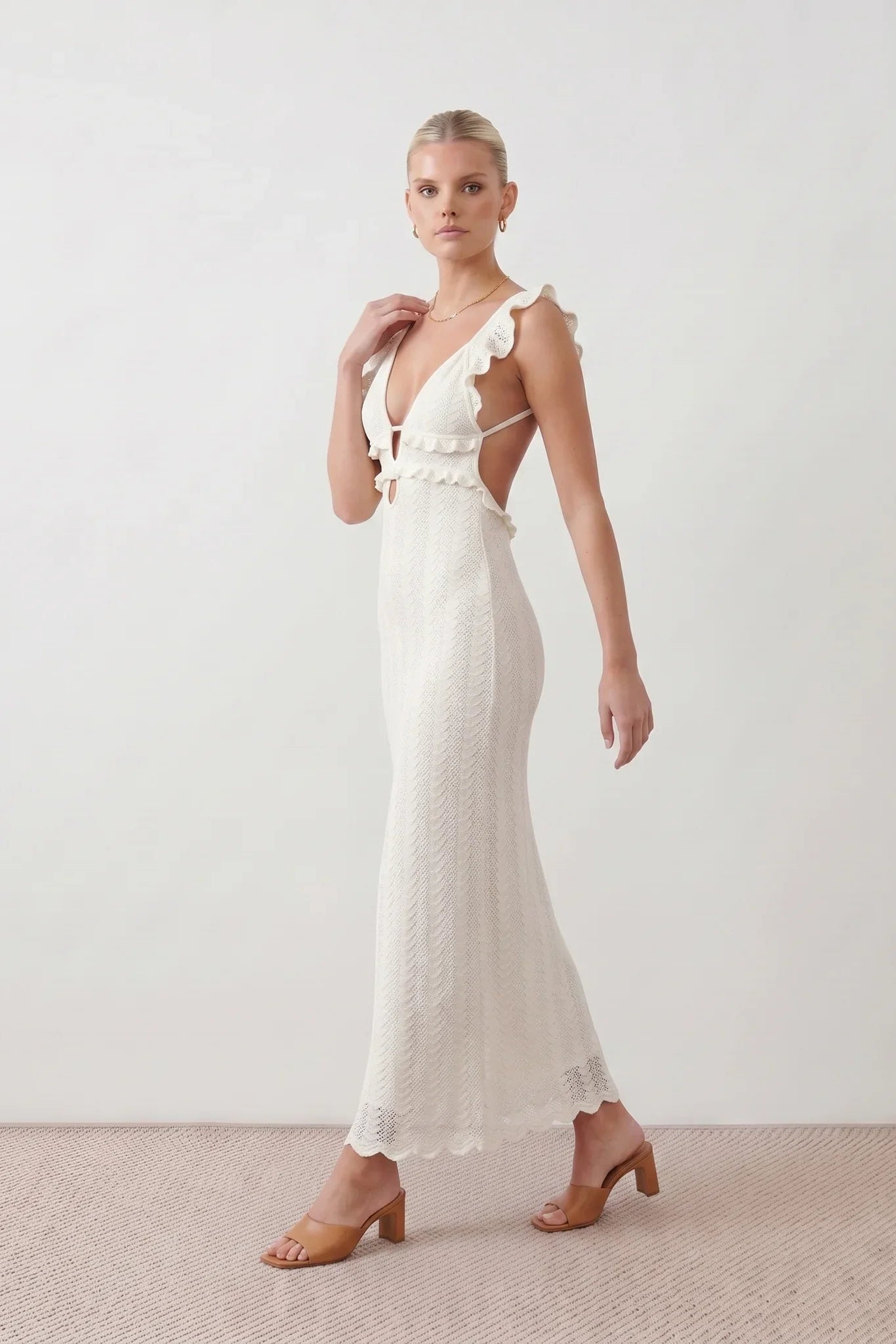Woman wearing the crochet mermaid maxi dress featuring an intricate crochet knit, plunging V-neckline, ruffled shoulder straps, keyhole waist cut-out, adjustable lace-up open back, scalloped hem, and a figure-hugging maxi silhouette, ideal for weddings, cocktail parties, and elegant evening occasions.