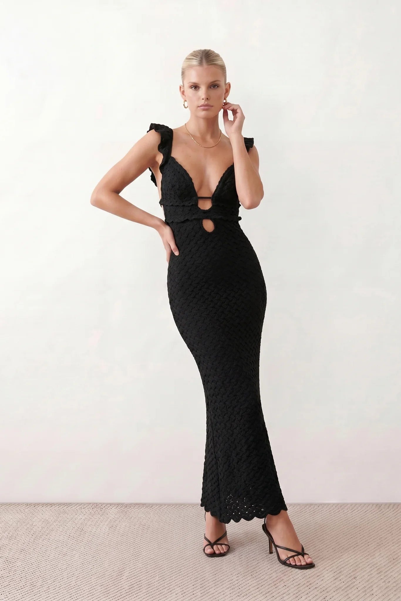 Woman wearing the crochet mermaid maxi dress featuring an intricate crochet knit, plunging V-neckline, ruffled shoulder straps, keyhole waist cut-out, adjustable lace-up open back, scalloped hem, and a figure-hugging maxi silhouette, ideal for weddings, cocktail parties, and elegant evening occasions.