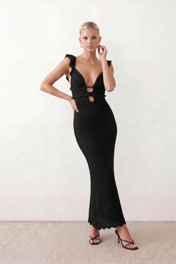 Woman wearing the crochet mermaid maxi dress featuring an intricate crochet knit, plunging V-neckline, ruffled shoulder straps, keyhole waist cut-out, adjustable lace-up open back, scalloped hem, and a figure-hugging maxi silhouette, ideal for weddings, cocktail parties, and elegant evening occasions.