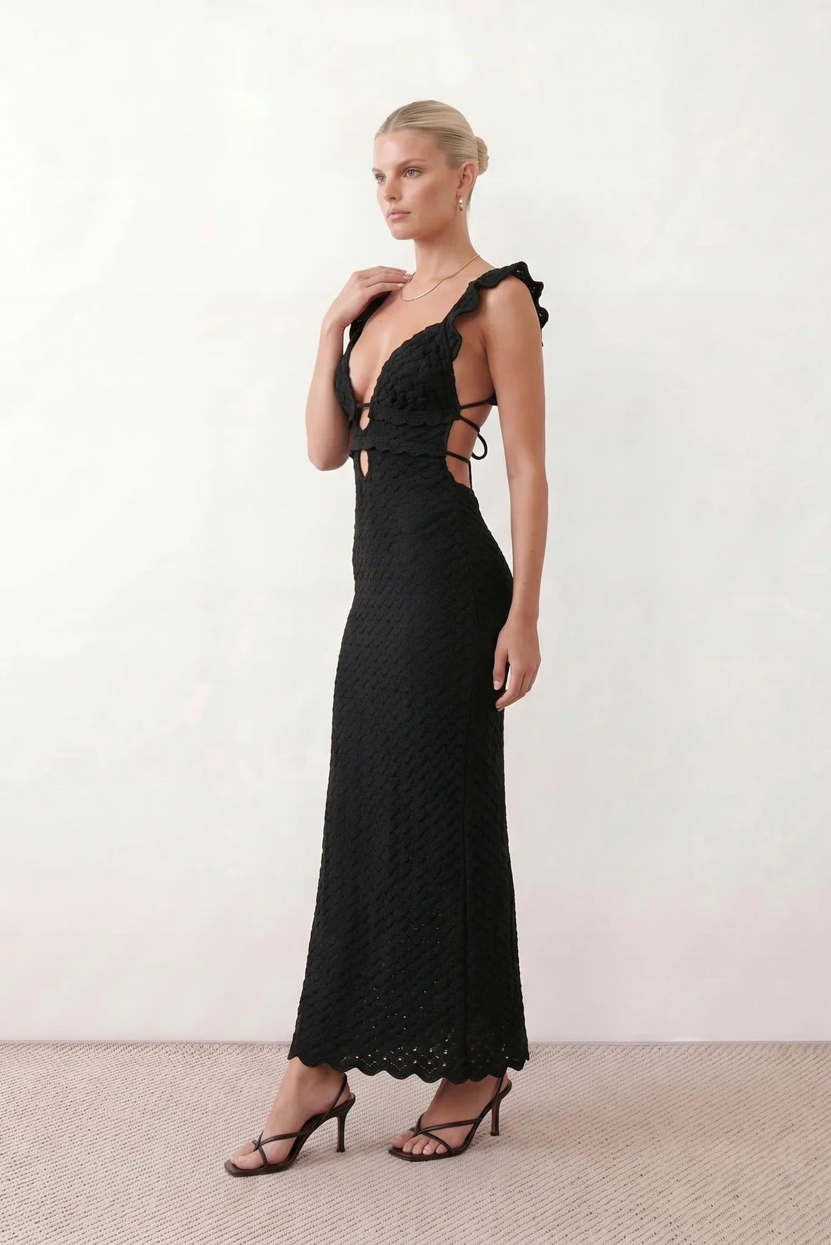 Woman wearing the crochet mermaid maxi dress featuring an intricate crochet knit, plunging V-neckline, ruffled shoulder straps, keyhole waist cut-out, adjustable lace-up open back, scalloped hem, and a figure-hugging maxi silhouette, ideal for weddings, cocktail parties, and elegant evening occasions.
