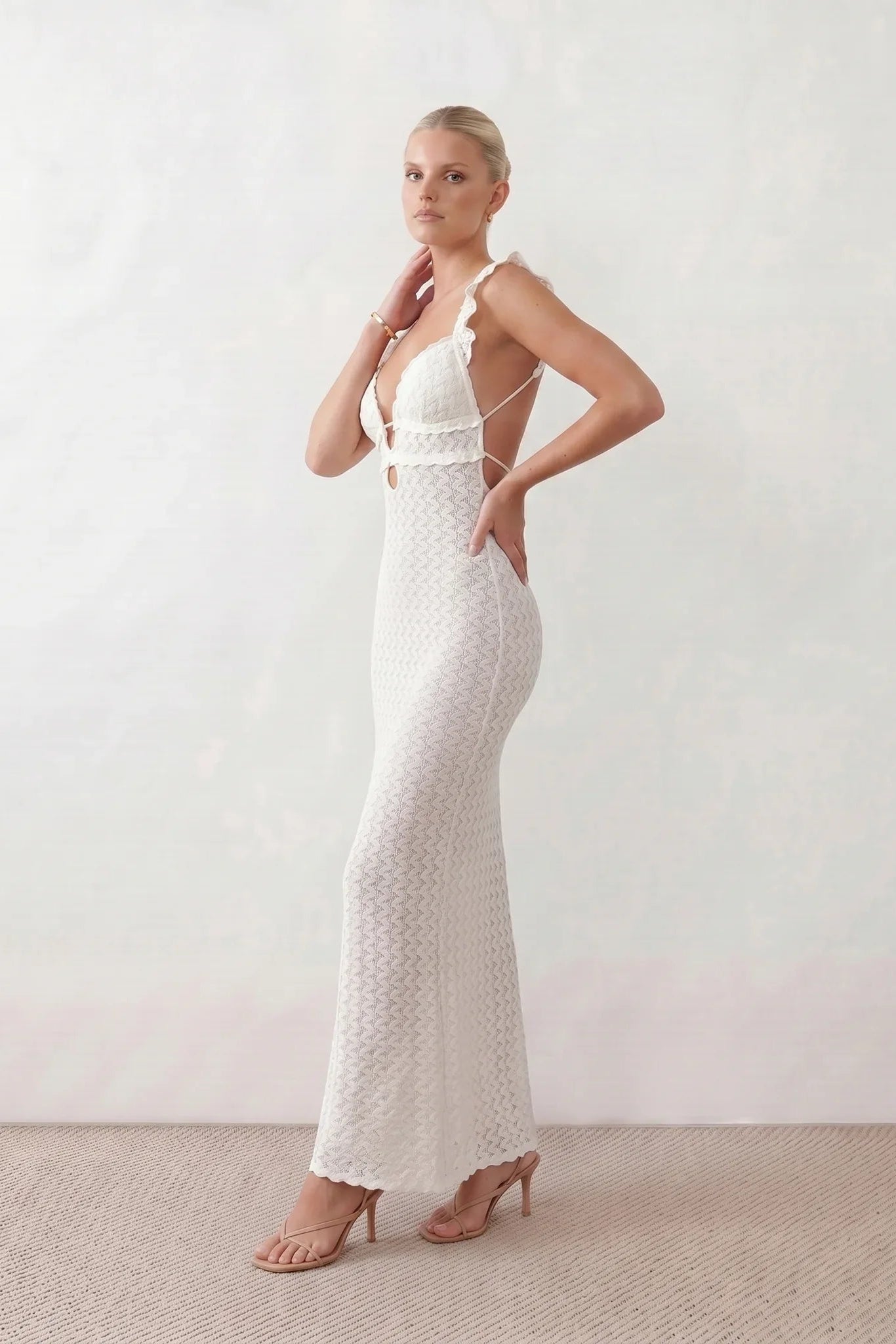 Woman wearing the crochet mermaid maxi dress featuring an intricate crochet knit, plunging V-neckline, ruffled shoulder straps, keyhole waist cut-out, adjustable lace-up open back, scalloped hem, and a figure-hugging maxi silhouette, ideal for weddings, cocktail parties, and elegant evening occasions.