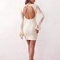 Woman wearing the Anahera open back fitted mini dress with sheer embroidered long sleeves, a round neckline, side cut-out details, and a sleek sheath silhouette, ideal for cocktail parties and evening occasions.