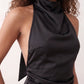 Woman wearing the Glossy Halter Mini Dress in a lustrous glossy finish, featuring a draped cowl halter neckline, open back with adjustable tie closure, side cut-out, ruched waist, and an A-line mini skirt, ideal for parties and evening occasions.