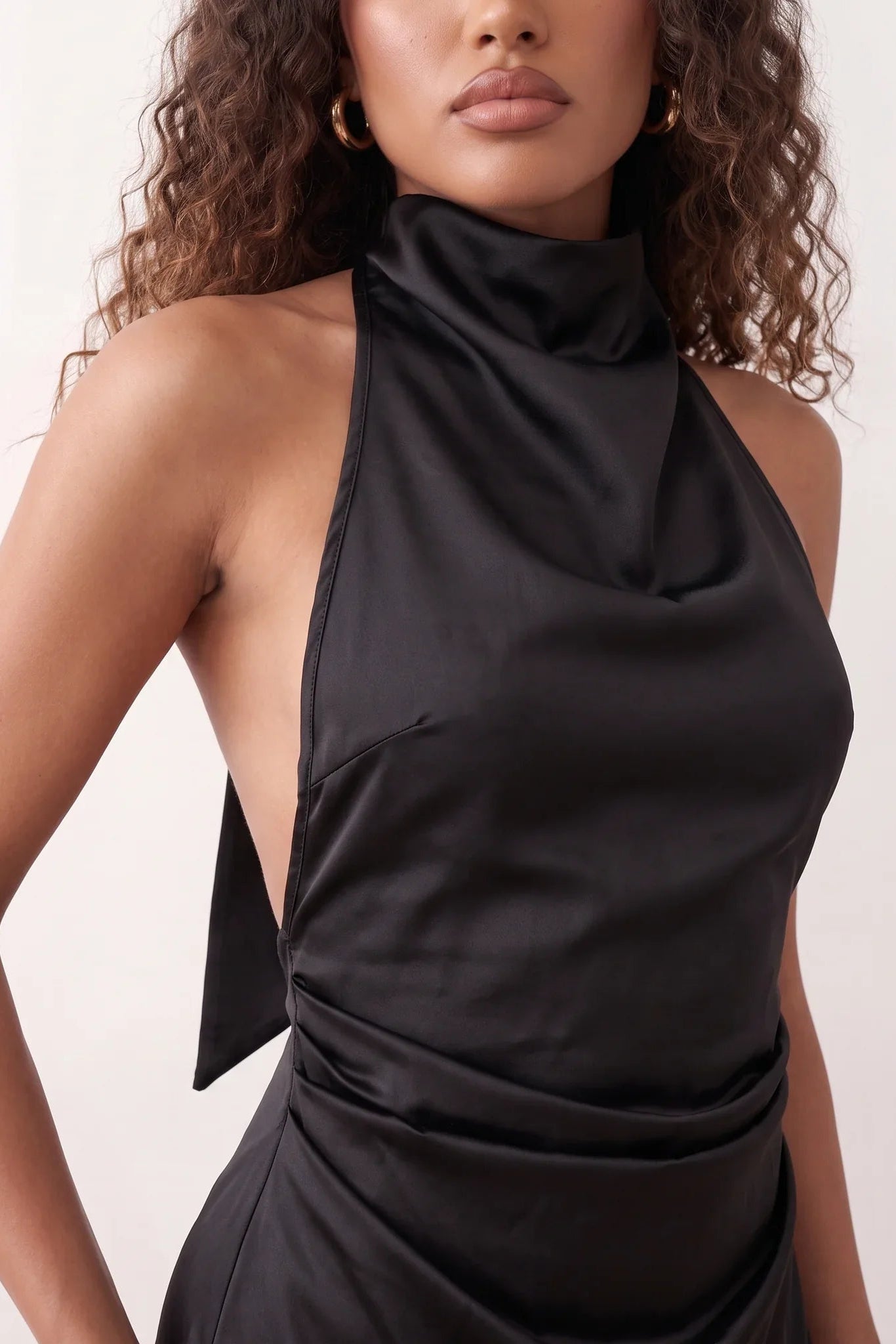 Woman wearing the Glossy Halter Mini Dress in a lustrous glossy finish, featuring a draped cowl halter neckline, open back with adjustable tie closure, side cut-out, ruched waist, and an A-line mini skirt, ideal for parties and evening occasions.
