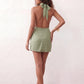 Woman wearing the Glossy Halter Mini Dress in a lustrous glossy finish, featuring a draped cowl halter neckline, open back with adjustable tie closure, side cut-out, ruched waist, and an A-line mini skirt, ideal for parties and evening occasions.