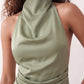 Woman wearing the Glossy Halter Mini Dress in a lustrous glossy finish, featuring a draped cowl halter neckline, open back with adjustable tie closure, side cut-out, ruched waist, and an A-line mini skirt, ideal for parties and evening occasions.