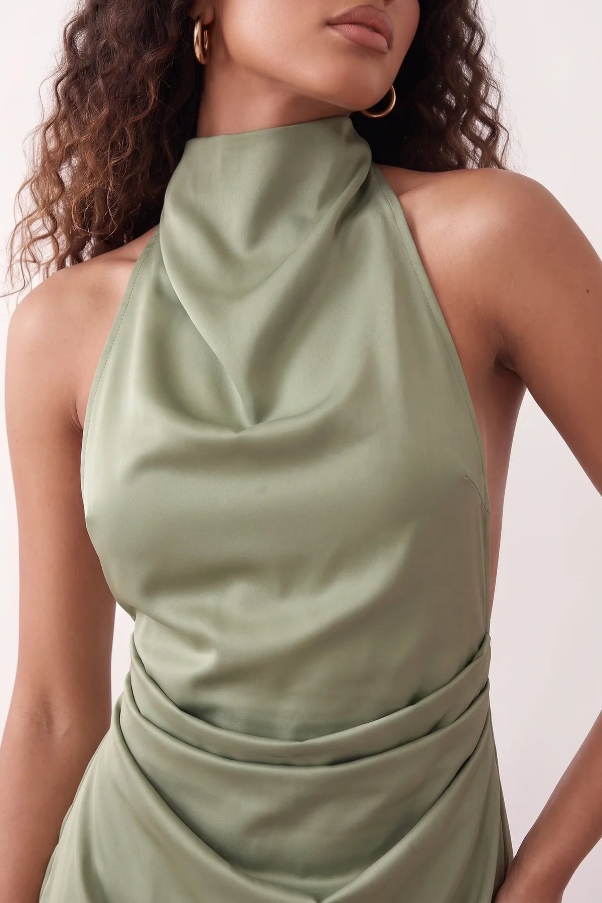 Woman wearing the Glossy Halter Mini Dress in a lustrous glossy finish, featuring a draped cowl halter neckline, open back with adjustable tie closure, side cut-out, ruched waist, and an A-line mini skirt, ideal for parties and evening occasions.