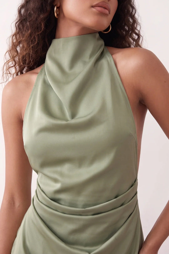 Woman wearing the Glossy Halter Mini Dress in a lustrous glossy finish, featuring a draped cowl halter neckline, open back with adjustable tie closure, side cut-out, ruched waist, and an A-line mini skirt, ideal for parties and evening occasions.