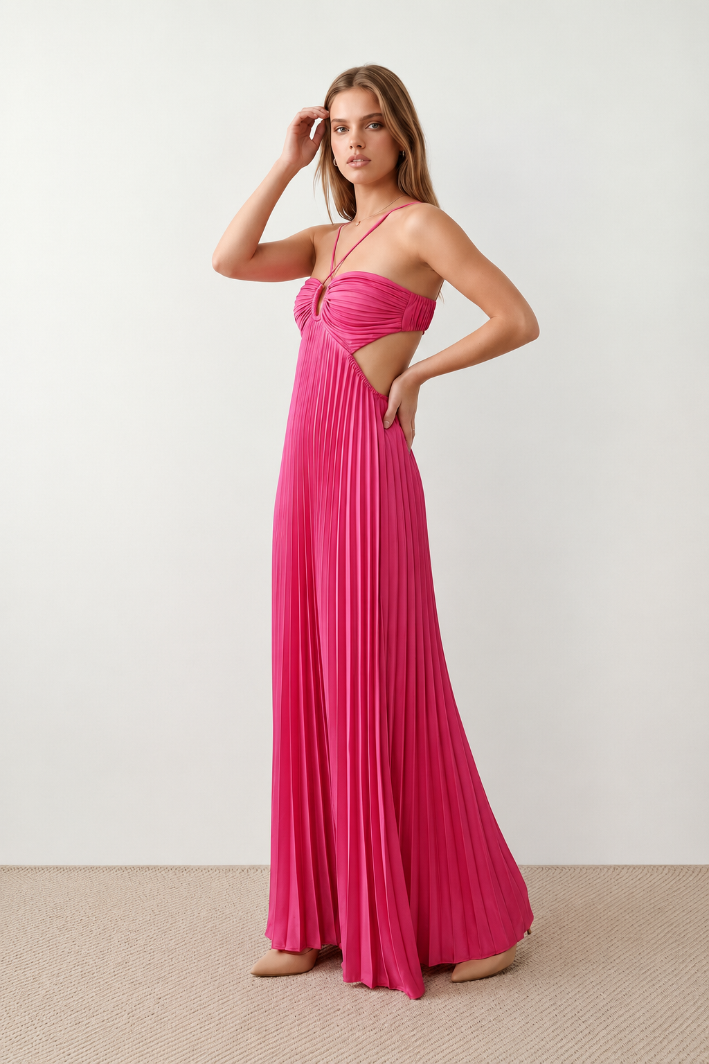 Woman wearing the Estella strapless pleated maxi dress featuring a ruched empire bodice, keyhole hardware detail, side cutout, open back with tie closure, and a flowing accordion-pleated floor-length skirt.