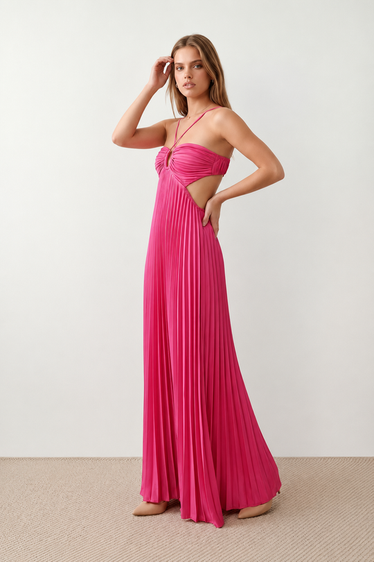Woman wearing the Estella strapless pleated maxi dress featuring a ruched empire bodice, keyhole hardware detail, side cutout, open back with tie closure, and a flowing accordion-pleated floor-length skirt.