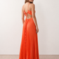Woman wearing the Estella strapless pleated maxi dress featuring a ruched empire bodice, keyhole hardware detail, side cutout, open back with tie closure, and a flowing accordion-pleated floor-length skirt.