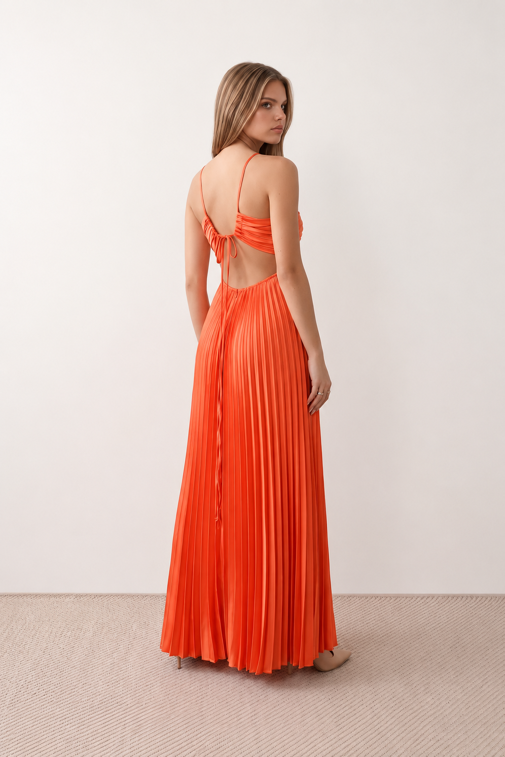Woman wearing the Estella strapless pleated maxi dress featuring a ruched empire bodice, keyhole hardware detail, side cutout, open back with tie closure, and a flowing accordion-pleated floor-length skirt.