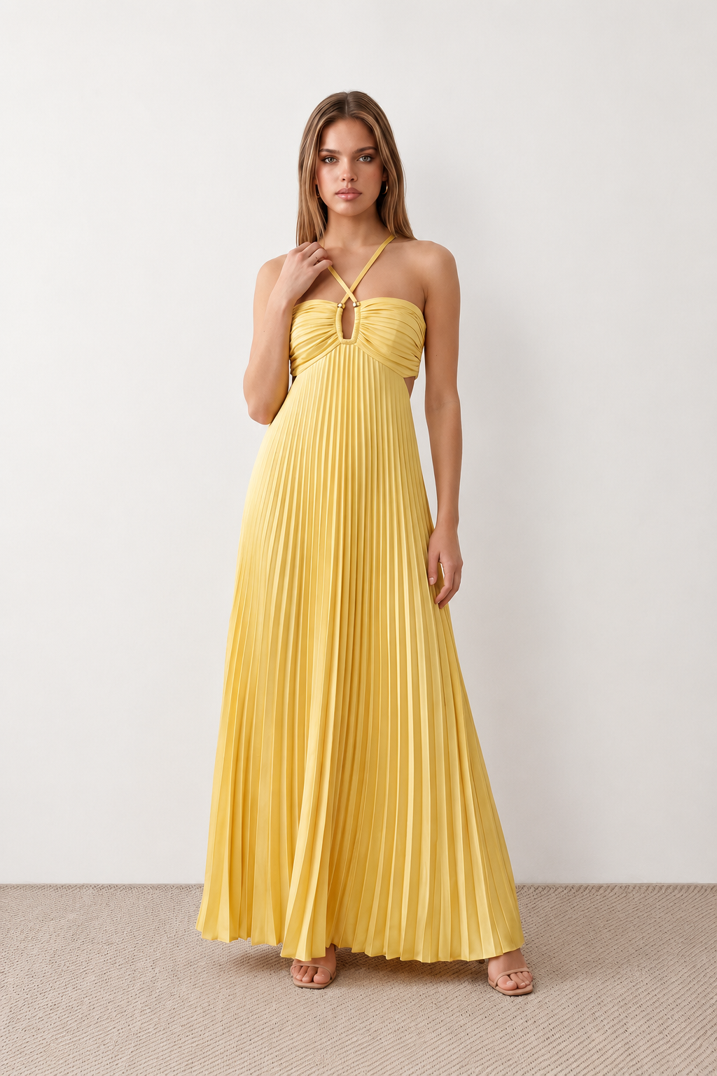 Woman wearing the Estella strapless pleated maxi dress featuring a ruched empire bodice, keyhole hardware detail, side cutout, open back with tie closure, and a flowing accordion-pleated floor-length skirt.