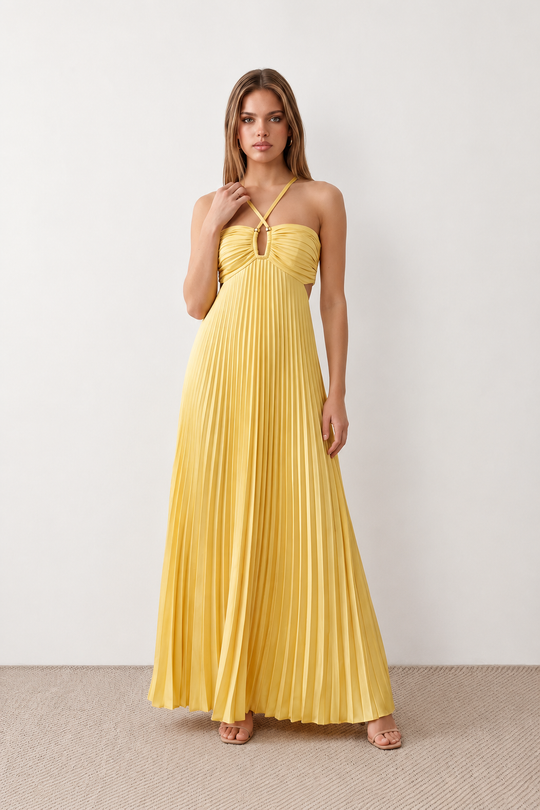 Woman wearing the Estella strapless pleated maxi dress featuring a ruched empire bodice, keyhole hardware detail, side cutout, open back with tie closure, and a flowing accordion-pleated floor-length skirt.