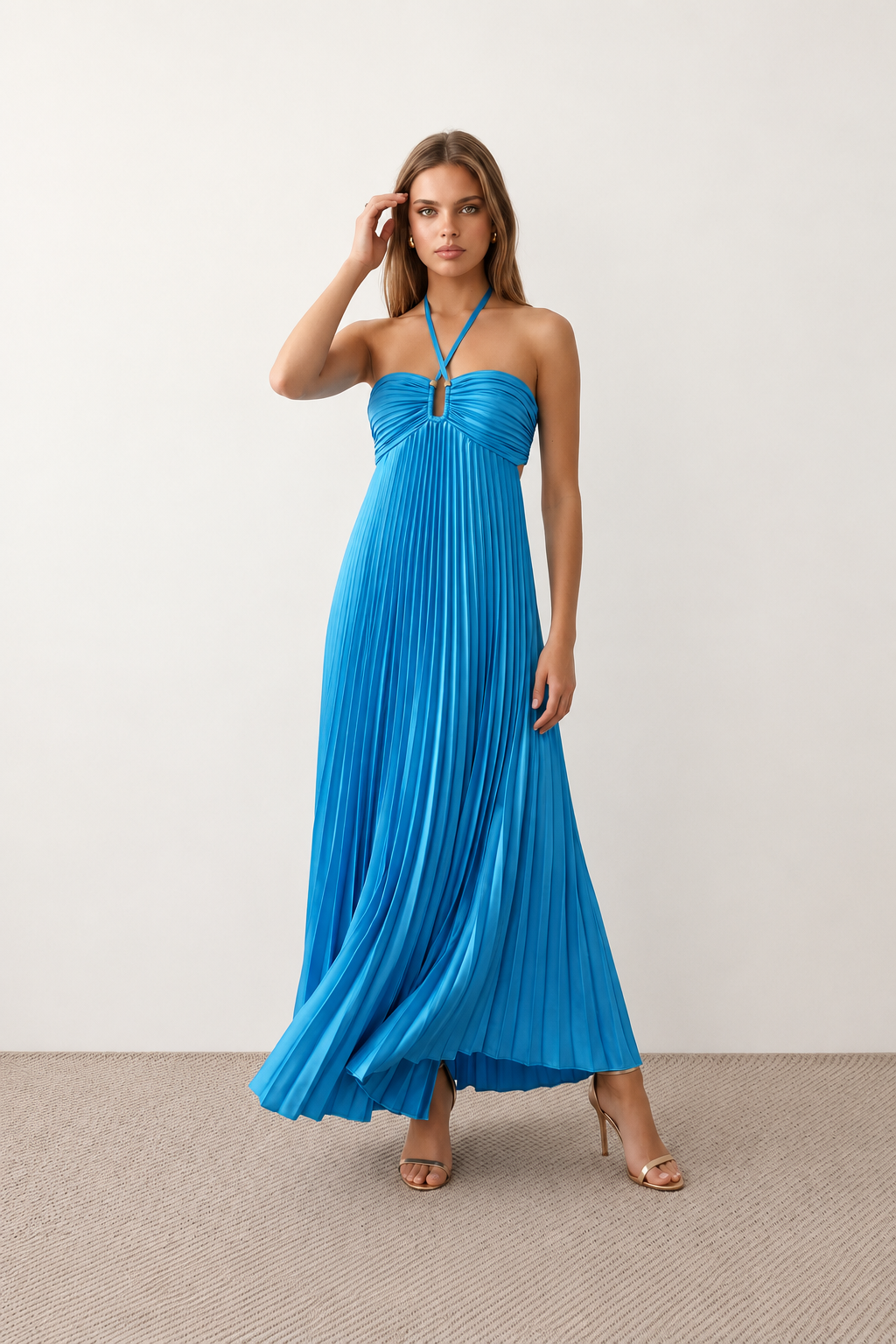 Woman wearing the Estella strapless pleated maxi dress featuring a ruched empire bodice, keyhole hardware detail, side cutout, open back with tie closure, and a flowing accordion-pleated floor-length skirt.