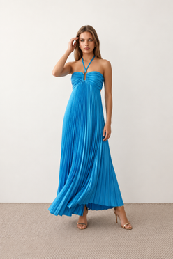 Woman wearing the Estella strapless pleated maxi dress featuring a ruched empire bodice, keyhole hardware detail, side cutout, open back with tie closure, and a flowing accordion-pleated floor-length skirt.