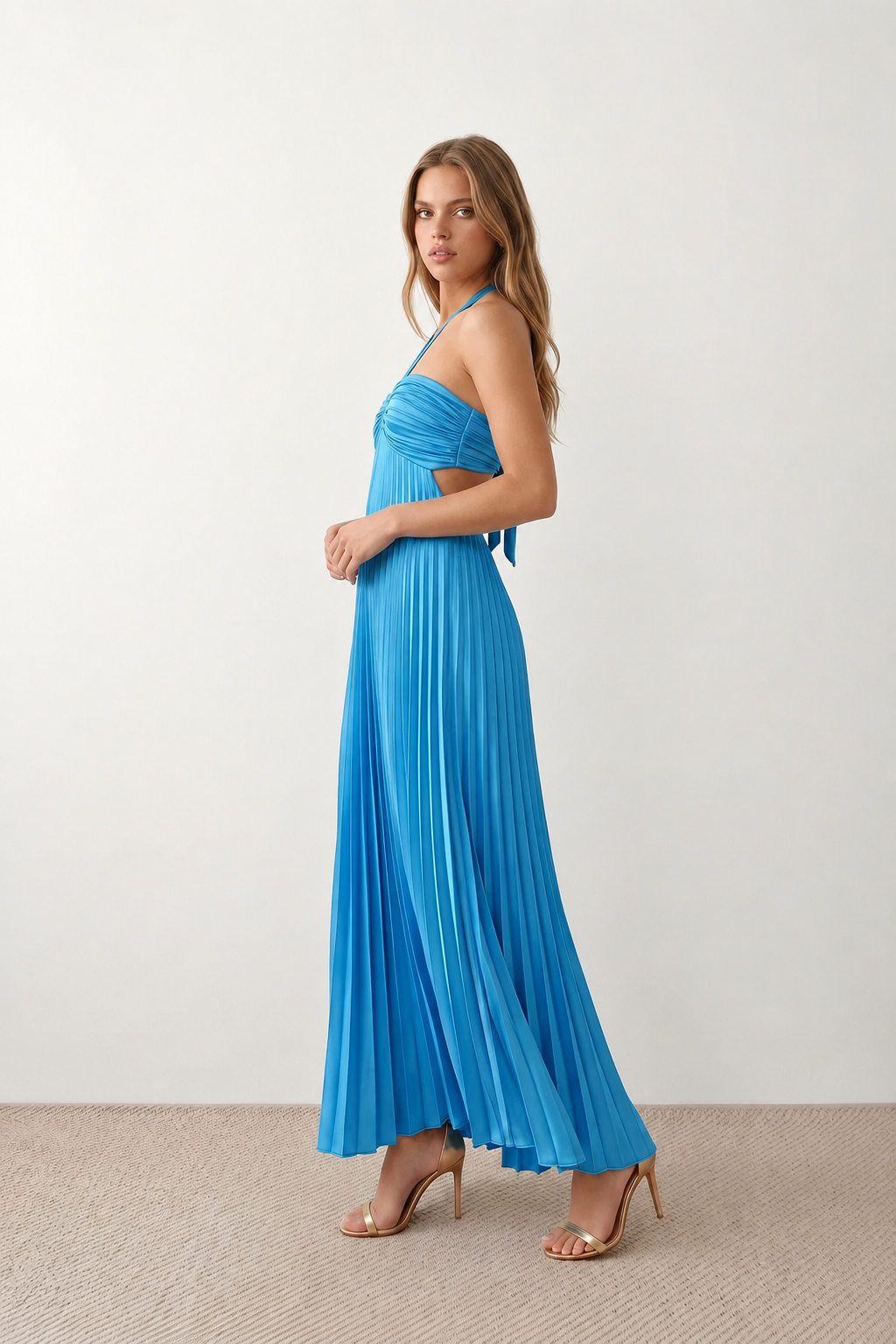 Woman wearing the Estella strapless pleated maxi dress featuring a ruched empire bodice, keyhole hardware detail, side cutout, open back with tie closure, and a flowing accordion-pleated floor-length skirt.