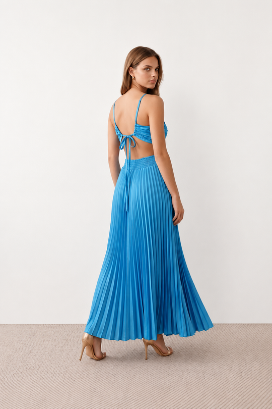 Woman wearing the Estella strapless pleated maxi dress featuring a ruched empire bodice, keyhole hardware detail, side cutout, open back with tie closure, and a flowing accordion-pleated floor-length skirt.