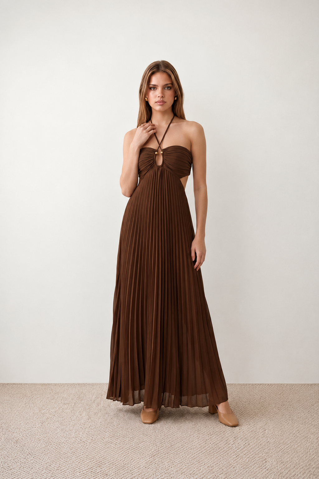Woman wearing the Estella strapless pleated maxi dress featuring a ruched empire bodice, keyhole hardware detail, side cutout, open back with tie closure, and a flowing accordion-pleated floor-length skirt.