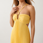 Woman wearing the Estella strapless pleated maxi dress featuring a ruched empire bodice, keyhole hardware detail, side cutout, open back with tie closure, and a flowing accordion-pleated floor-length skirt.