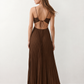 Woman wearing the Estella strapless pleated maxi dress featuring a ruched empire bodice, keyhole hardware detail, side cutout, open back with tie closure, and a flowing accordion-pleated floor-length skirt.