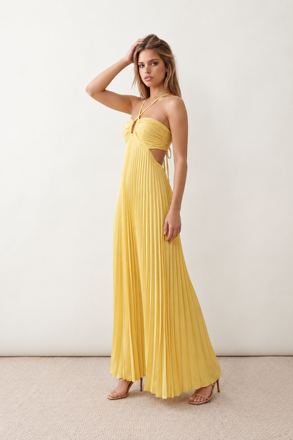 Woman wearing the Estella strapless pleated maxi dress featuring a ruched empire bodice, keyhole hardware detail, side cutout, open back with tie closure, and a flowing accordion-pleated floor-length skirt.