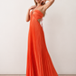 Woman wearing the Estella strapless pleated maxi dress featuring a ruched empire bodice, keyhole hardware detail, side cutout, open back with tie closure, and a flowing accordion-pleated floor-length skirt.