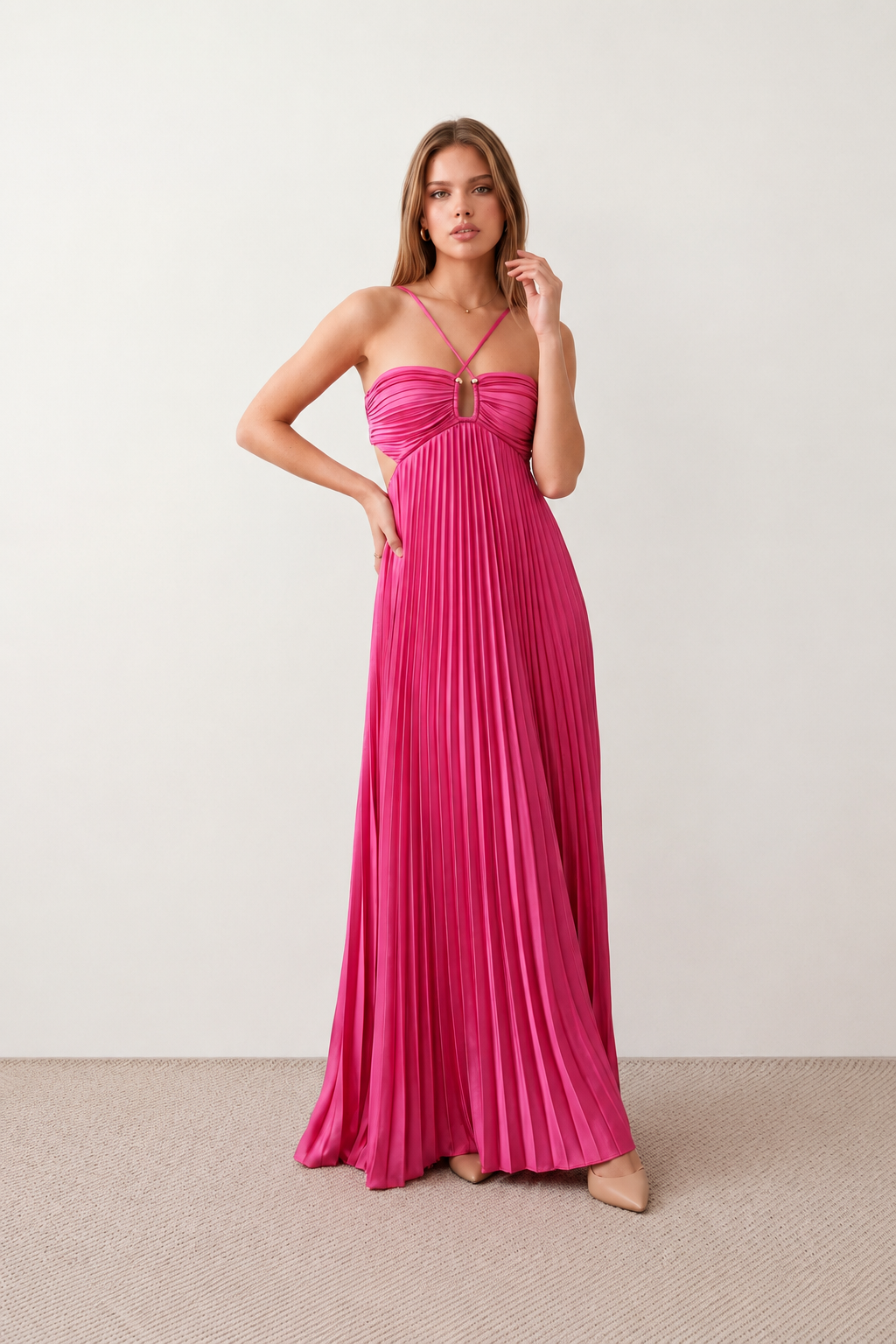 Woman wearing the Estella strapless pleated maxi dress featuring a ruched empire bodice, keyhole hardware detail, side cutout, open back with tie closure, and a flowing accordion-pleated floor-length skirt.