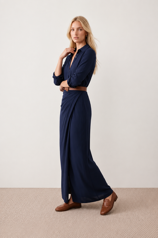 Woman wearing the Julieta Button Front Maxi Dress with a deep V-neck, shirt collar, button-front bodice, long sleeves, belted waist with a square-buckle belt, asymmetric pleated hip drape, and flowing maxi-length skirt.