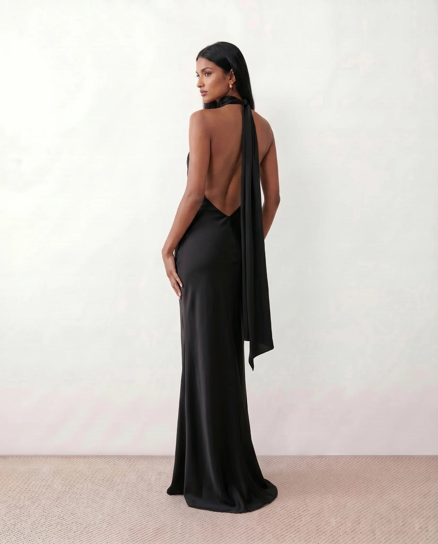 Woman wearing the Winnie satin halter maxi dress featuring a glossy satin finish, halter neckline with tie-back detail, open draped back, and a floor-length relaxed silhouette.