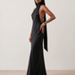 Woman wearing the Winnie satin halter maxi dress featuring a glossy satin finish, halter neckline with tie-back detail, open draped back, and a floor-length relaxed silhouette.