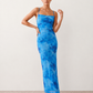 Seren spaghetti strap maxi dress in an abstract floral print featuring a square neckline, thin straps, a low lace-up open back, a shirred waist, and a fitted floor-length silhouette.