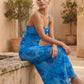 Seren spaghetti strap maxi dress in an abstract floral print featuring a square neckline, thin straps, a low lace-up open back, a shirred waist, and a fitted floor-length silhouette.