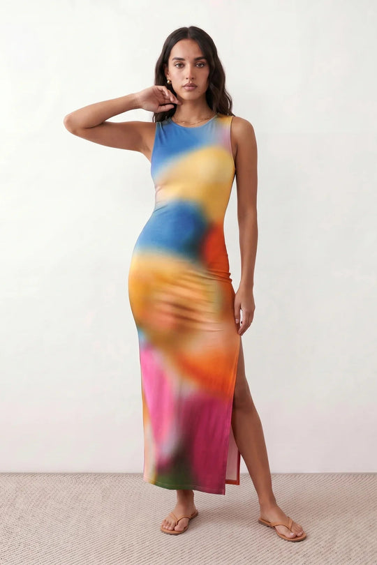 Woman wearing the abstract print side slit maxi dress in a vibrant multicolour tie-dye design, featuring a sleeveless round neckline, body-skimming column silhouette, thigh-high side slit, and full-length flowing skirt, ideal for summer holidays, weddings, and occasion wear.