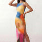 Woman wearing the abstract print side slit maxi dress in a vibrant multicolour tie-dye design, featuring a sleeveless round neckline, body-skimming column silhouette, thigh-high side slit, and full-length flowing skirt, ideal for summer holidays, weddings, and occasion wear.