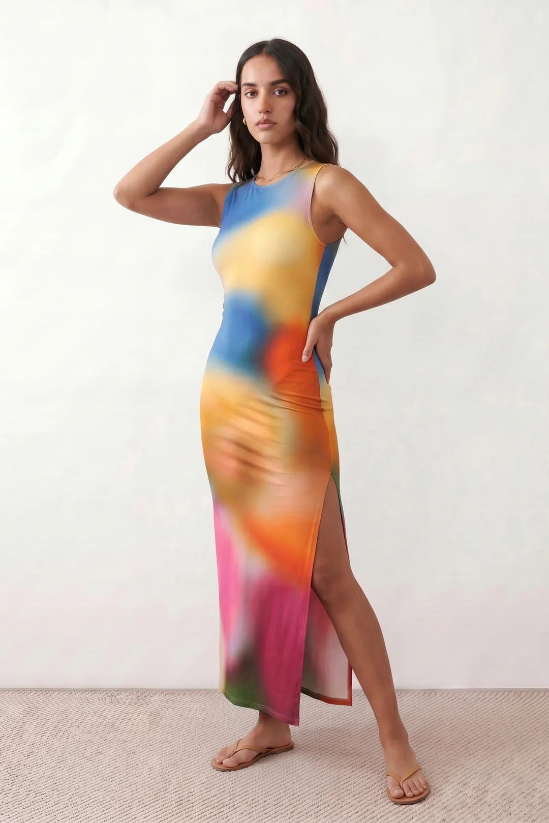 Woman wearing the abstract print side slit maxi dress in a vibrant multicolour tie-dye design, featuring a sleeveless round neckline, body-skimming column silhouette, thigh-high side slit, and full-length flowing skirt, ideal for summer holidays, weddings, and occasion wear.