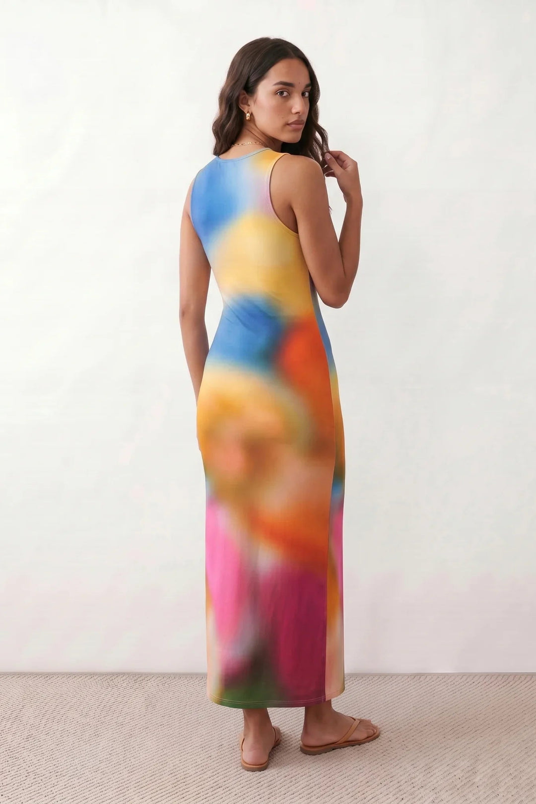 Woman wearing the Calia abstract print side slit maxi dress in a vibrant multicolour tie-dye design, featuring a sleeveless round neckline, body-skimming column silhouette, thigh-high side slit, and full-length flowing skirt, ideal for summer holidays, weddings, and occasion wear.