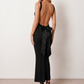 Woman wearing the Aline Cowl Neck Backless Maxi Dress in a floor-length fitted silhouette with a draped cowl neckline, elegant open back, oversized satin bow tie detail, sleeveless design, and smooth woven fabric, ideal for weddings, black-tie events, galas, and evening occasions.
