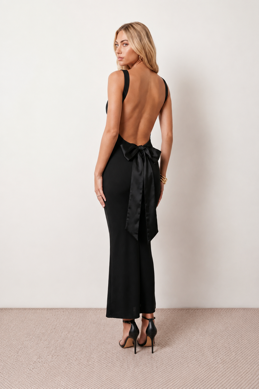 Woman wearing the Aline Cowl Neck Backless Maxi Dress in a floor-length fitted silhouette with a draped cowl neckline, elegant open back, oversized satin bow tie detail, sleeveless design, and smooth woven fabric, ideal for weddings, black-tie events, galas, and evening occasions.