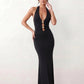 Woman wearing the Ariadna Mermaid Halter Maxi Dress featuring a deep plunge halter neckline, open back with adjustable tie fastening, gold-tone hardware at the ruched waist, subtle waist cut-out and a floor-length mermaid silhouette, ideal for weddings, black-tie events and formal evening occasions.
