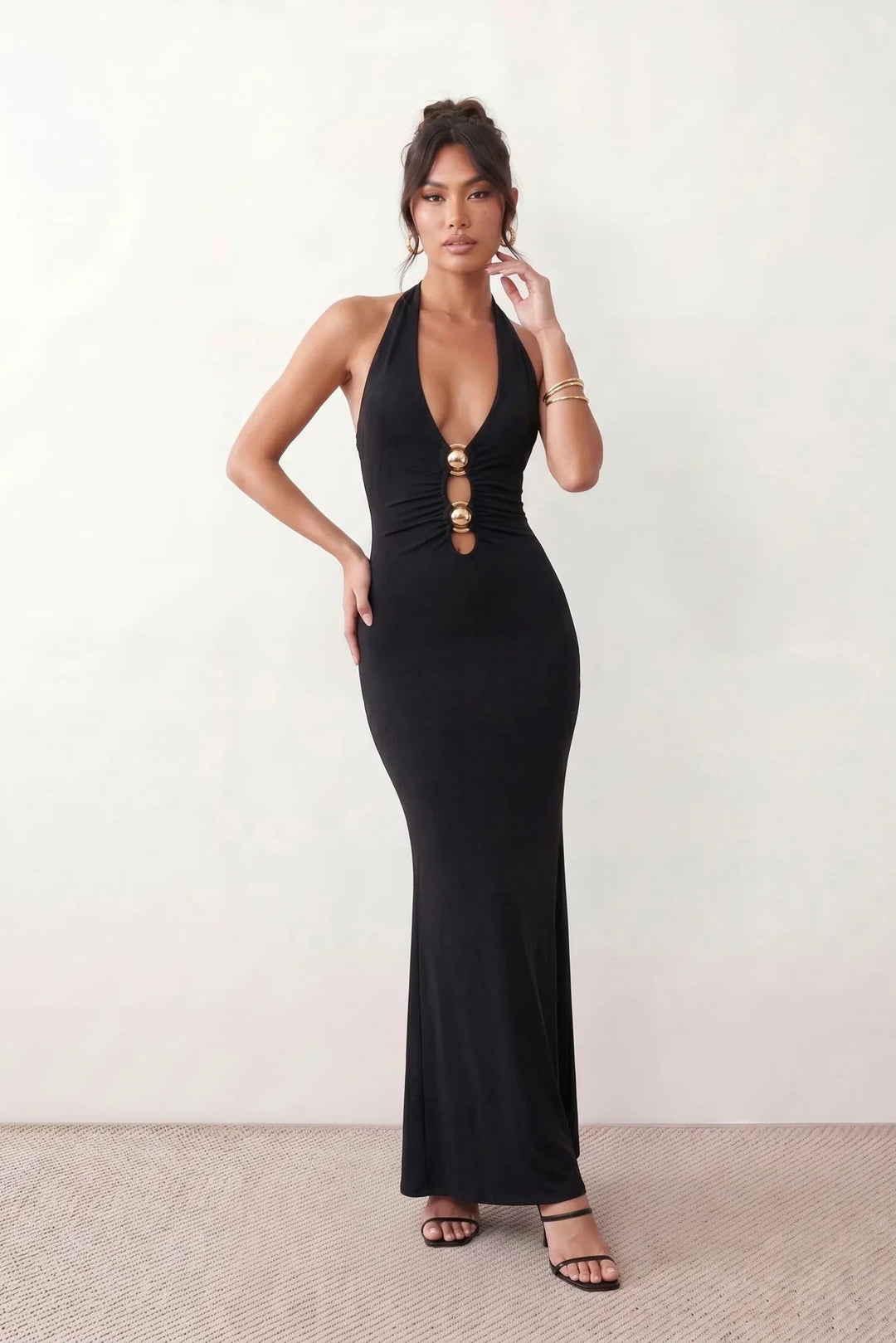 Woman wearing the Ariadna Mermaid Halter Maxi Dress featuring a deep plunge halter neckline, open back with adjustable tie fastening, gold-tone hardware at the ruched waist, subtle waist cut-out and a floor-length mermaid silhouette, ideal for weddings, black-tie events and formal evening occasions.
